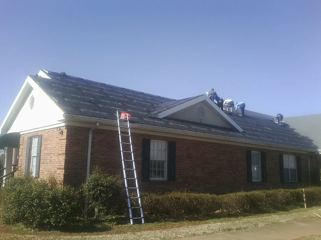Crew tearing shingles off a brick ranch roof with a ladder set — Emergency Roof Repair work by our crew in Parlin