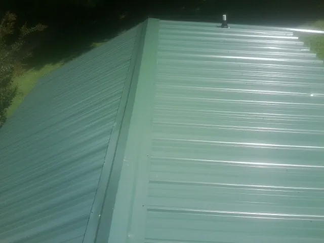 New green metal panels meeting at the ridge of a roof — Flat Roof Repair work by our crew in Parlin