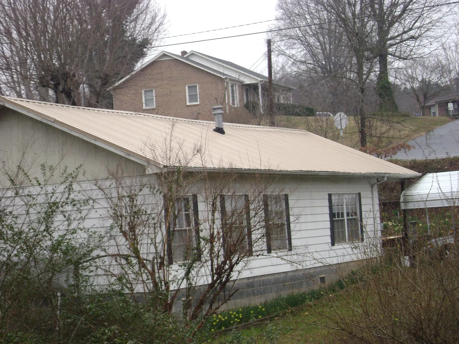 Tan metal roof on a white sided house set into a hillside — Commercial Roofing by Roofing Brothers in Parlin